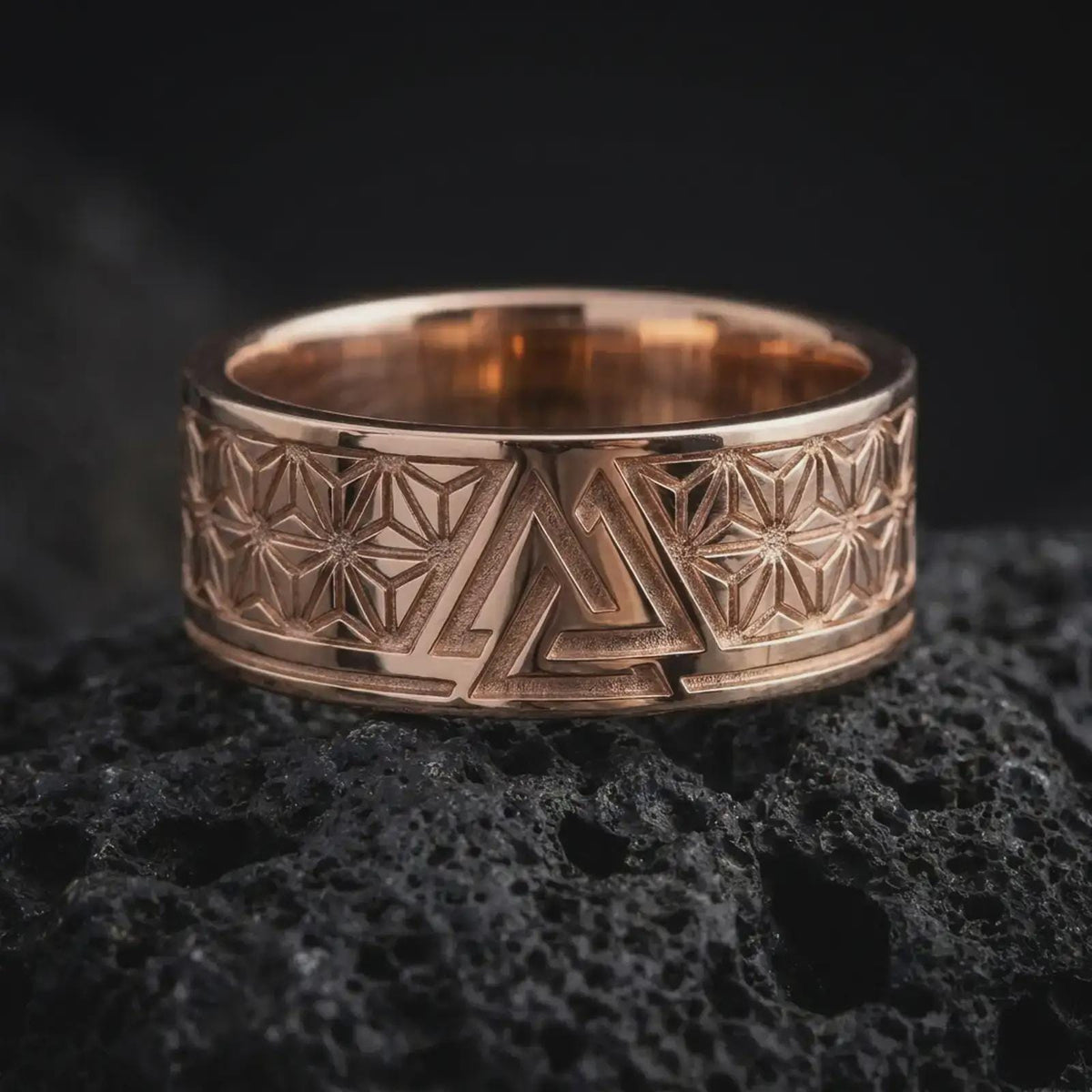 Rose Gold Plated Valknut ring resting on black volcanic rock, showing the wide band, raised borders, and detailed Asanoha-inspired patterns.
