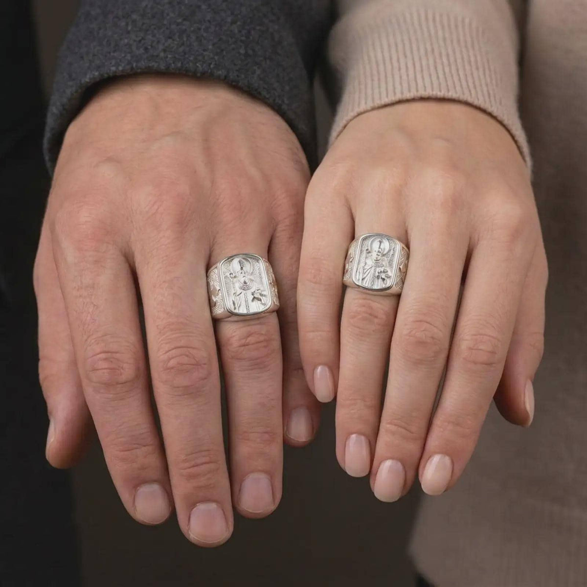 Polished 925 sterling silver matching St Nicholas of Myra rings worn on the fingers of a man and woman together, showcasing detailed Catholic bishop figures, ornate religious vestments, three-ball books, rectangular signet frames, and bright polished silver finishes.