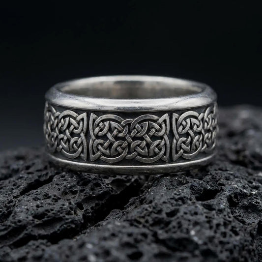 Oxidized 925 sterling silver Celtic knot ring displayed on textured black volcanic rock, featuring continuous interwoven Celtic knotwork, raised silver patterns, dark recessed details, smooth rounded edges, and oxidized silver finish.