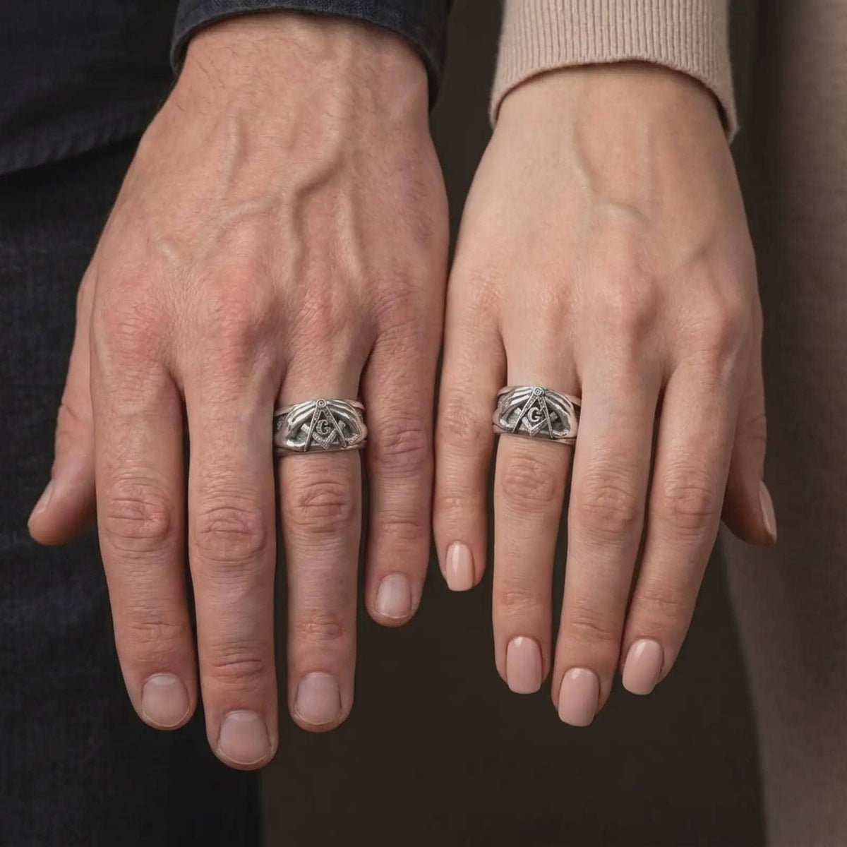 Polished 925 sterling silver matching Masonic rings worn on the fingers of a man and woman together, showcasing detailed symmetrical hands, raised square and compass symbols, central G letters, and matching bright polished silver finishes.