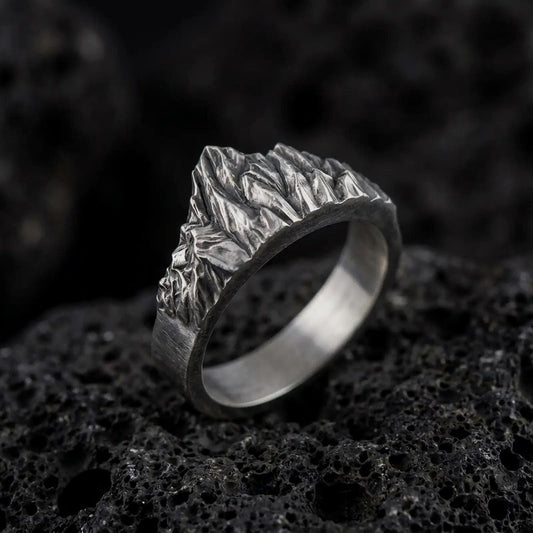 Oxidized 925 sterling silver mountain range ring displayed on textured black volcanic rock, featuring sculpted alpine peaks, jagged mountain ridges, detailed rocky slopes, an irregular summit silhouette, and dark oxidized silver finish.