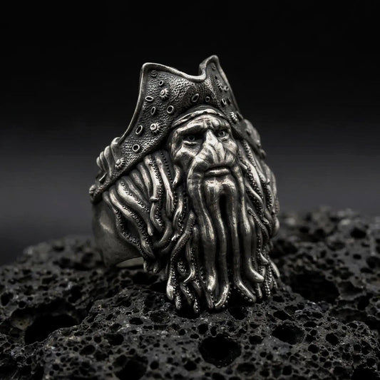Oxidized 925 sterling silver Davy Jones pirate ring displayed on textured black volcanic rock, featuring a weathered sea captain face, barnacle-like details on a tricorn hat, flowing octopus tentacle beard with suction cups, and dark oxidized silver finish.