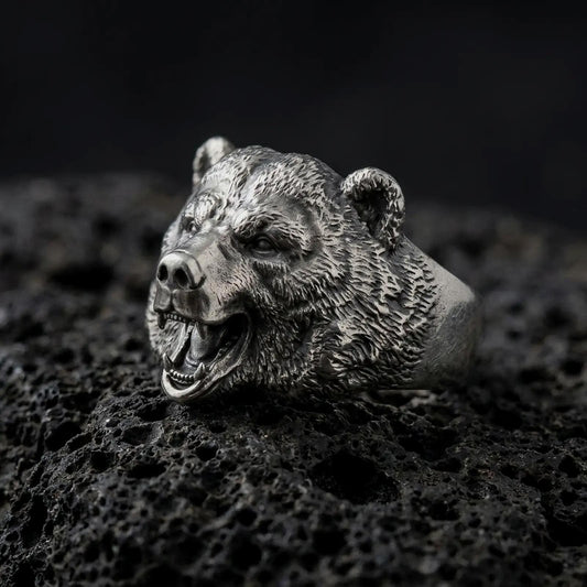 Oxidized 925 sterling silver roaring bear head ring displayed on textured black volcanic rock, featuring a realistic three-dimensional bear face, wide open mouth, exposed sharp fangs, detailed fur, rounded ears, and dark oxidized silver finish.