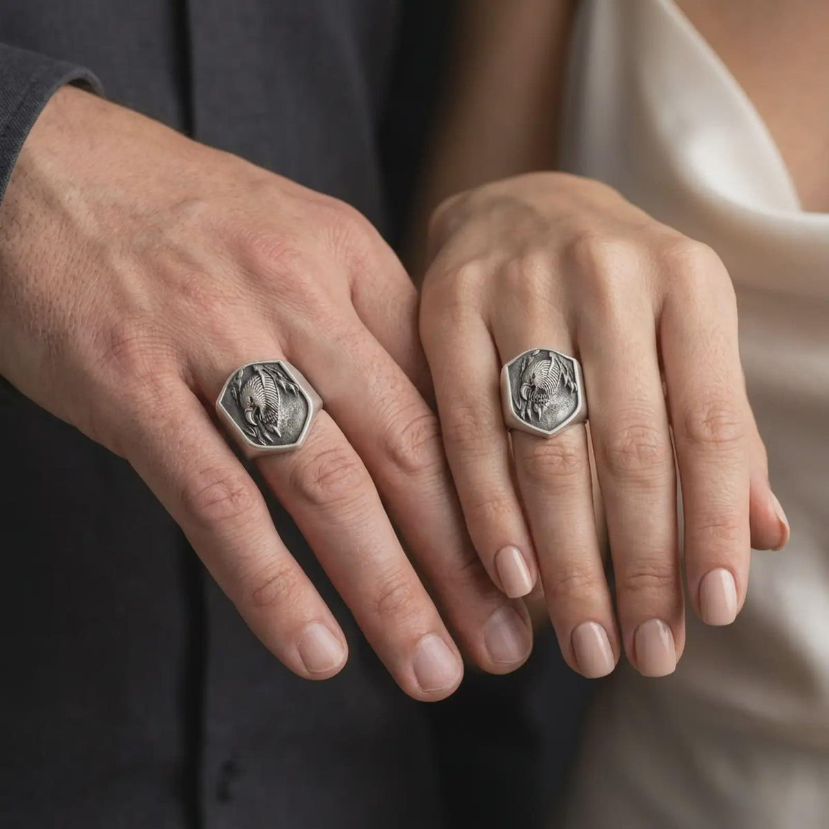 Oxidized 925 sterling silver matching eagle head signet rings worn on the fingers of a man and woman together, featuring fierce screaming eagle portraits, open hooked beaks, detailed feathers, sharp talons, and coordinated dark oxidized silver finishes.