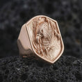 Load image into Gallery viewer, Rose gold plated 925 sterling silver eagle head ring resting on black volcanic stone, highlighting the three-dimensional screaming eagle portrait, layered feathers, curved talons, dark textured shield background, and rose gold plated finish.
