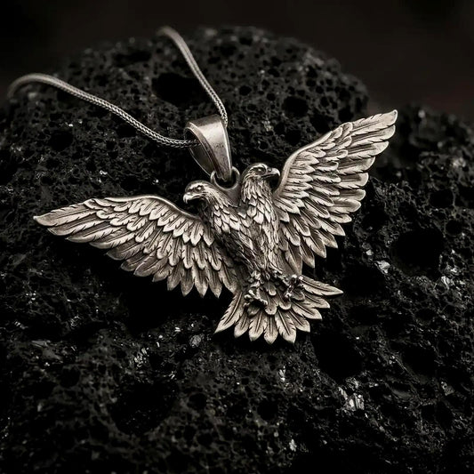 Oxidized 925 sterling silver double headed eagle pendant displayed on textured black volcanic rock, featuring two opposing eagle heads, fully spread wings, detailed layered feathers, and a dark oxidized silver finish.