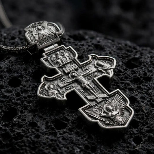 Oxidized 925 sterling silver Russian Orthodox cross pendant displayed on black volcanic rock, featuring the Crucifixion of Jesus, miniature saint portraits, religious inscriptions, ornate cross borders, and dark oxidized silver finish.