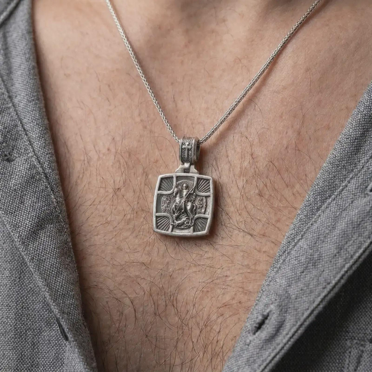 Oxidized Silver Saint George Slaying Dragon pendant worn on a man's chest with an open black shirt, showcasing its detailed Orthodox icon relief.