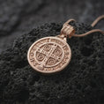 Load image into Gallery viewer, Rose Gold Plated Saint Benedict religious pendant on black volcanic rock, showing the circular Benedict medal design with symbolic inscriptions.

