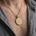 Load image into Gallery viewer, Gold Plated double sided Saint Benedict pendant worn on a man's chest with an open black shirt, emphasizing its religious medal design.

