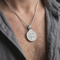 Load image into Gallery viewer, Polished Silver Saint Benedict necklace displayed on a man's chest, highlighting the round Catholic medal and cross-detailed bail.
