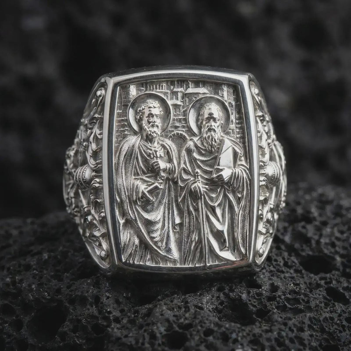 Polished Silver Saint Peter and Paul ring on black volcanic rock, highlighting the rectangular signet face, architectural background, and ornate side engravings.