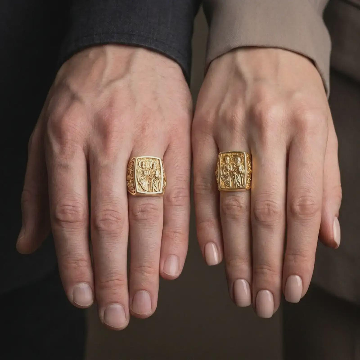 Gold Plated Saint Peter and Paul rings displayed on the fingers of a man and woman together, featuring the rectangular Catholic signet design.