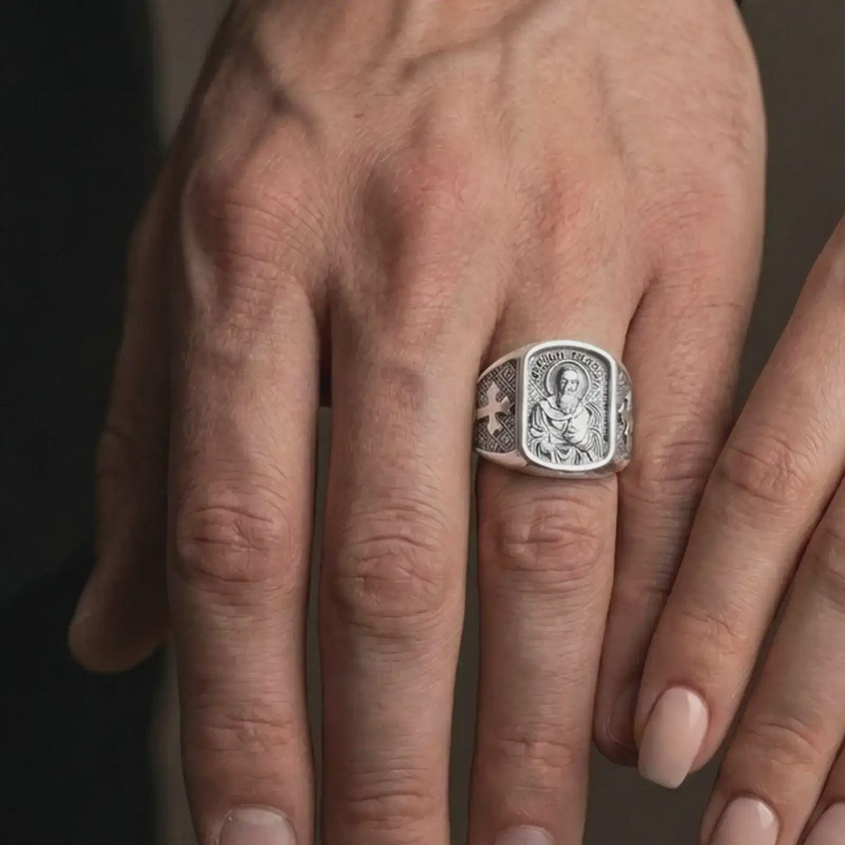 Polished Silver Saint Paul signet rings worn by a man and woman together, highlighting the rectangular religious relief and geometric side patterns.