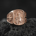 Load image into Gallery viewer, Rose Gold Plated Saint Paul Catholic signet ring resting on black volcanic rock, featuring sculpted robes, a traditional halo, and ornate cross engravings.
