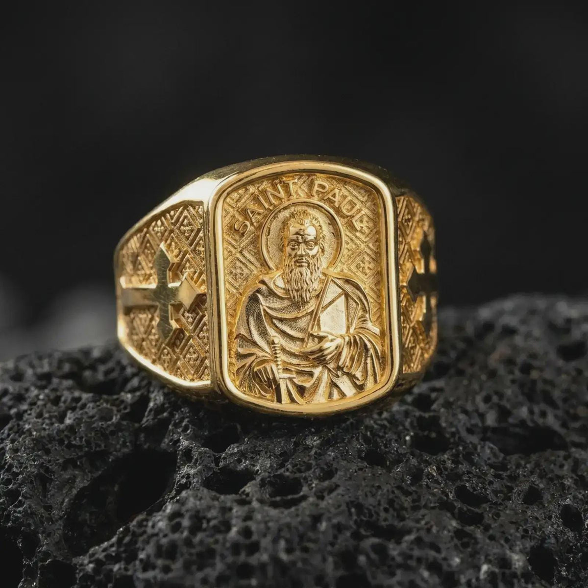 Gold Plated Saint Paul Apostle ring displayed on black volcanic rock, showcasing the raised side crosses and decorative diamond-patterned band.