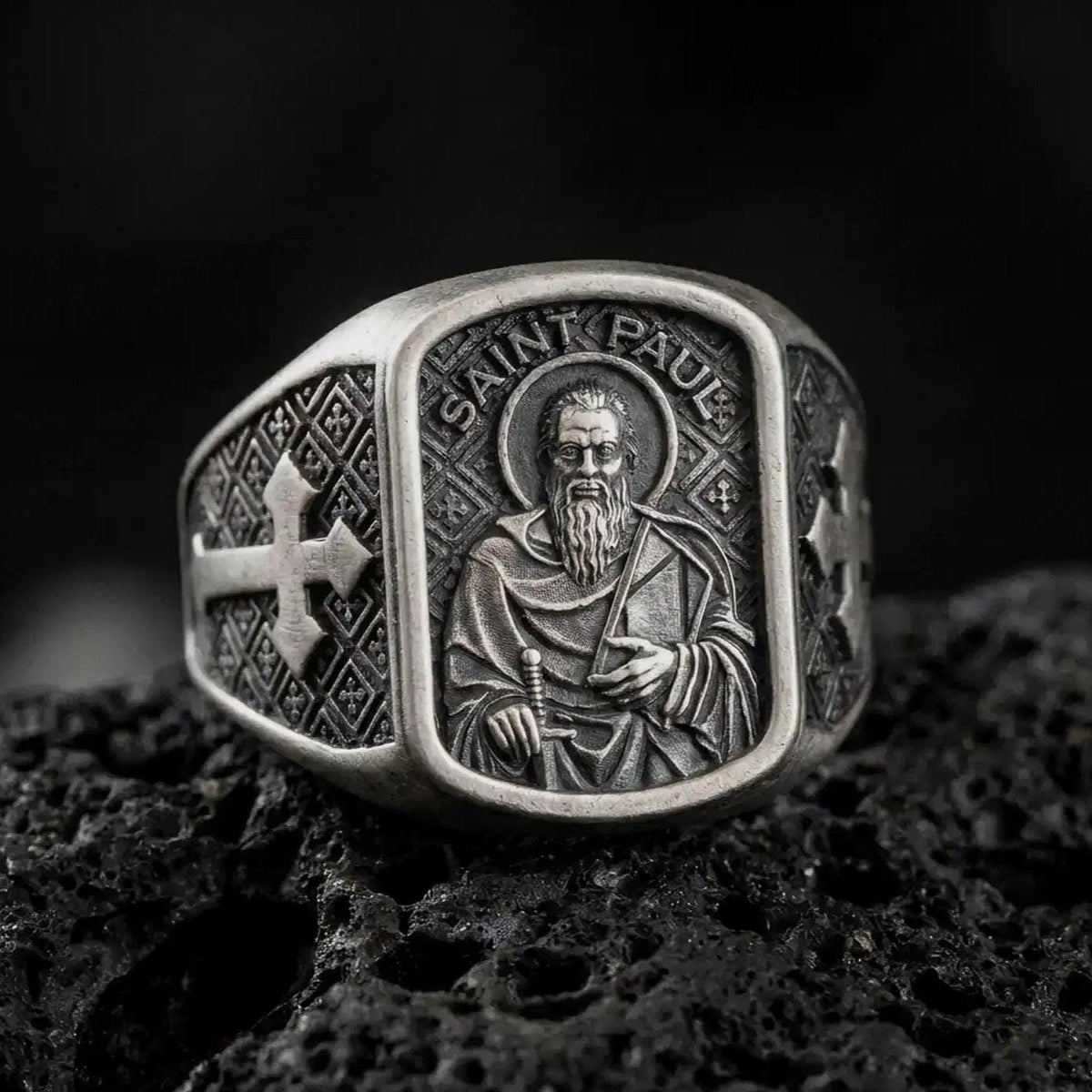 Oxidized Silver Saint Paul Apostle signet ring on black volcanic rock, featuring the haloed saint holding a sword and book in detailed relief.