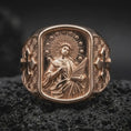 Load image into Gallery viewer, Rose Gold Plated Saint Cecilia religious signet ring resting on black volcanic rock, featuring flowing robes, musical symbolism, and decorative side crosses.
