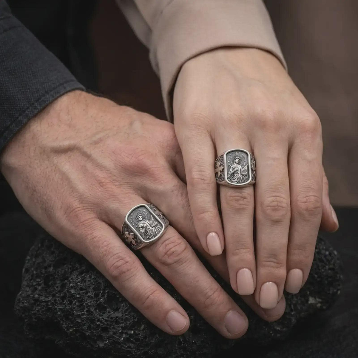 Oxidized Silver Saint Cecilia rings worn on the fingers of a man and woman together, showcasing the detailed saint portraits and cross-decorated bands.