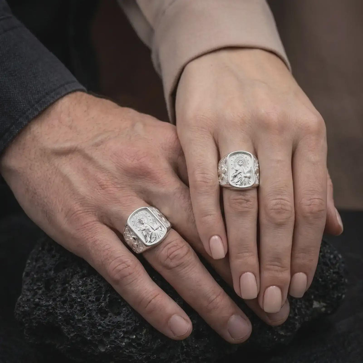 Polished Silver Saint Cecilia signet rings worn by a man and woman together, highlighting the musical instrument, starry halo, and geometric engravings.