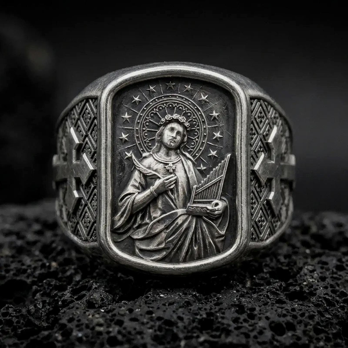 Oxidized Silver Saint Cecilia signet ring on black volcanic rock, featuring the patron saint of musicians holding a portable organ and martyr's palm.